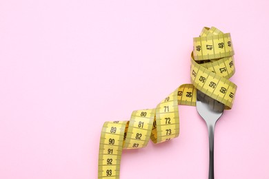 Photo of Fork with measuring tape on pink background, top view and space for text. Diet concept