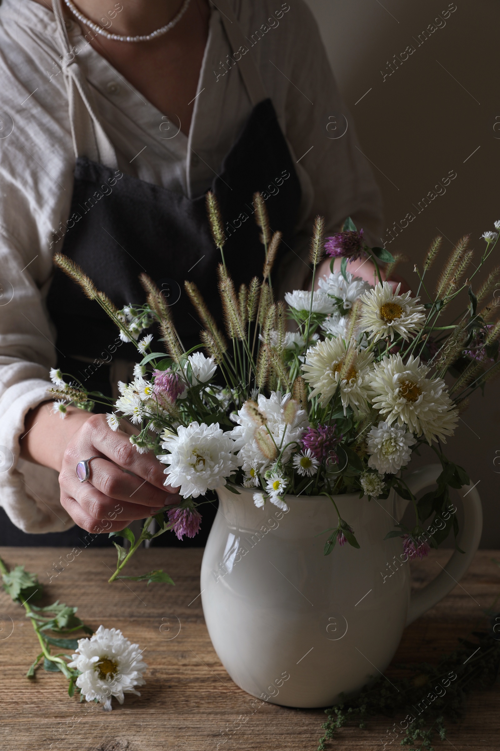 Photo of Woman creating beautiful flower arrangement at wooden table, closeup