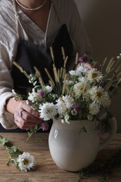 Photo of Woman creating beautiful flower arrangement at wooden table, closeup