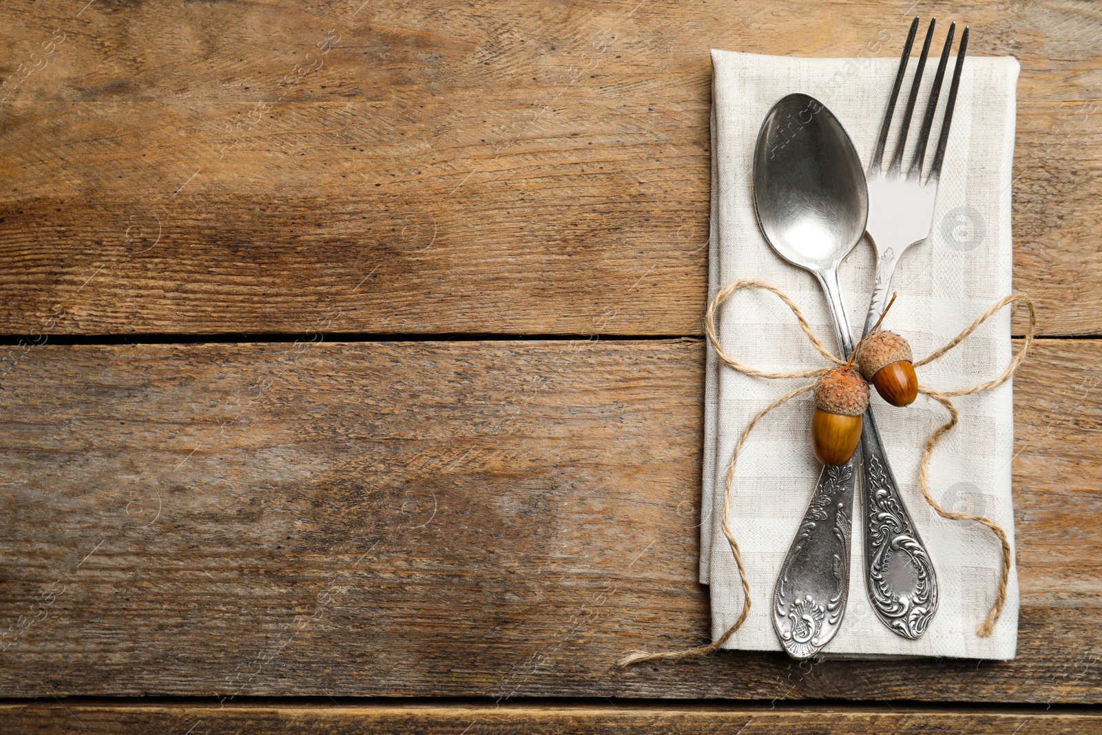Photo of Autumn table setting, space for text. Cutlery with napkin and acorns on wooden background, top view