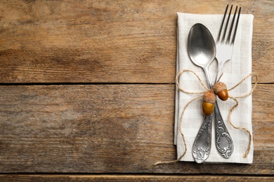 Autumn table setting, space for text. Cutlery with napkin and acorns on wooden background, top view