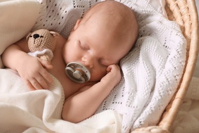 Photo of Cute newborn baby sleeping on white blanket in wicker crib, closeup