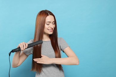 Photo of Beautiful woman using hair iron on light blue background, space for text