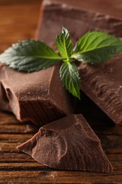 Photo of Pieces of tasty milk chocolate and mint on wooden table, closeup