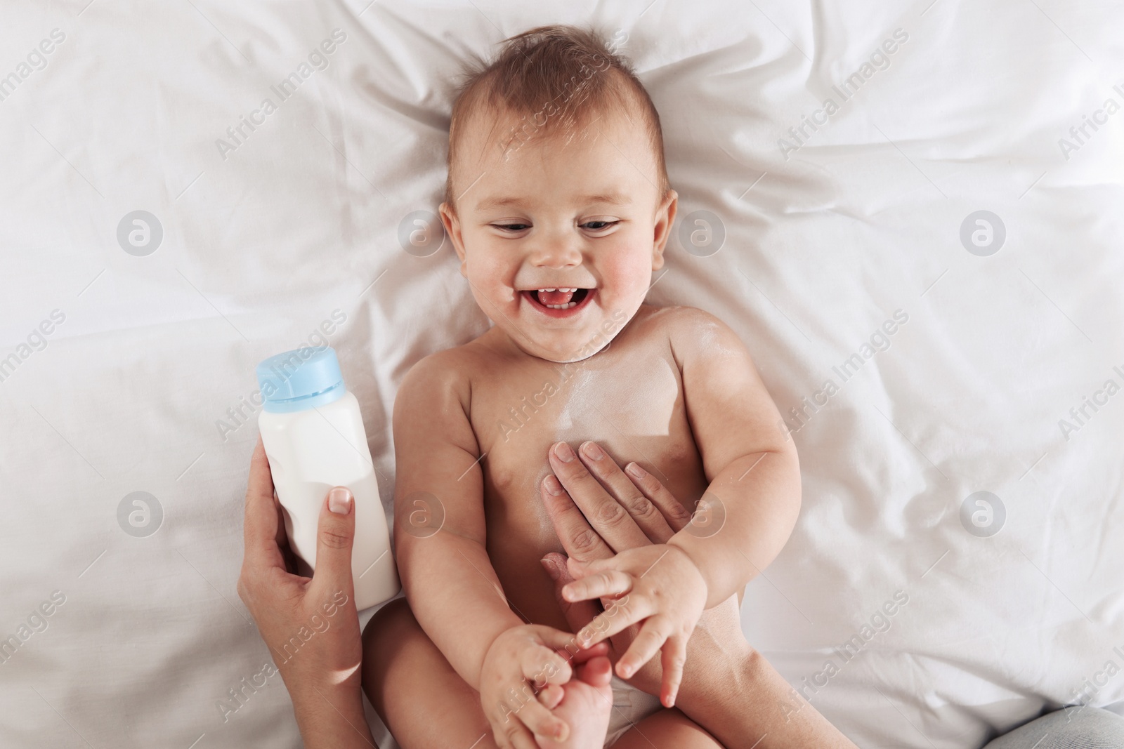 Photo of Mother applying dusting powder onto her baby on bed, top view