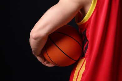 Photo of Athletic man with basketball ball on black background, closeup