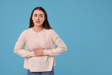 Photo of Woman suffering from abdominal pain on light blue background, space for text. Unhealthy stomach