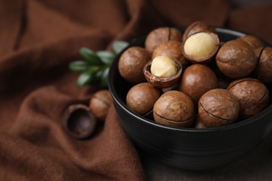 Tasty Macadamia nuts in bowl on table, closeup. Space for text