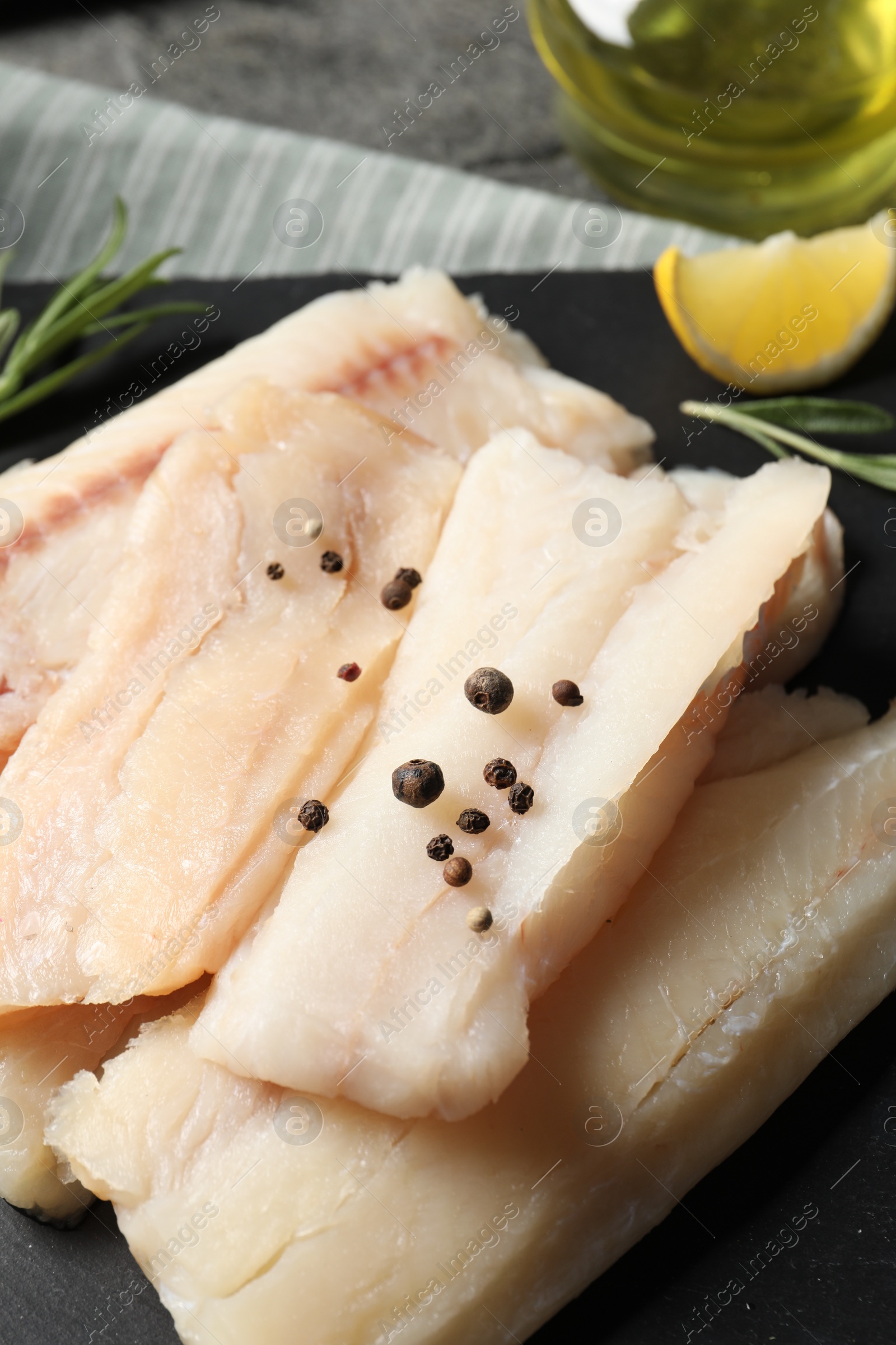 Photo of Pieces of raw cod fish and peppercorns on table, closeup