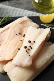 Pieces of raw cod fish and peppercorns on table, closeup