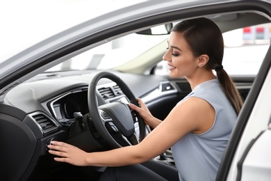 Young woman sitting in driver's seat of new car at salon