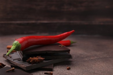 Photo of Delicious chocolate, fresh red chili peppers and spices on grey textured table, closeup. Space for text