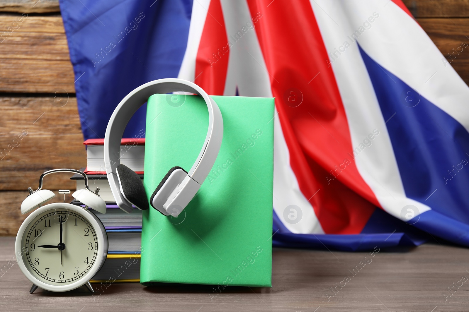 Photo of Learning foreign language. Different books, headphones and alarm clock on wooden table near flag of United Kingdom, space for text