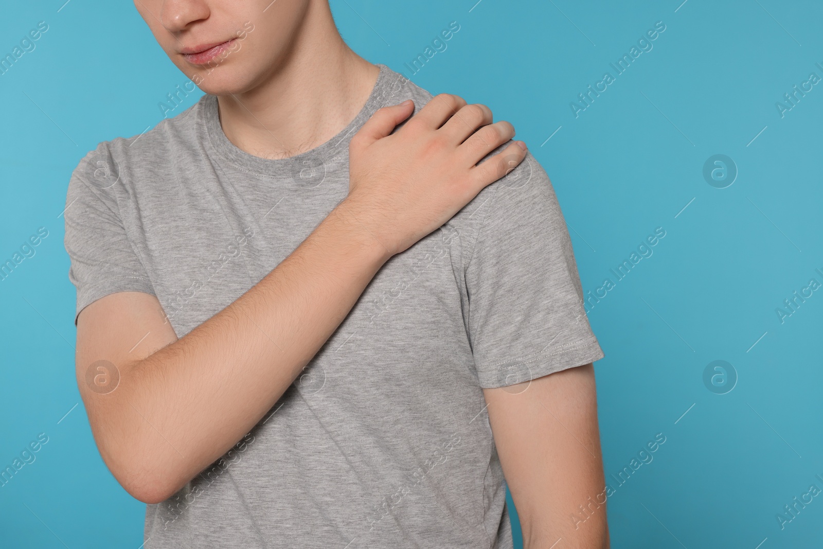 Photo of Man suffering from pain in his shoulder on light blue background, closeup. Arthritis symptoms