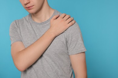 Man suffering from pain in his shoulder on light blue background, closeup. Arthritis symptoms