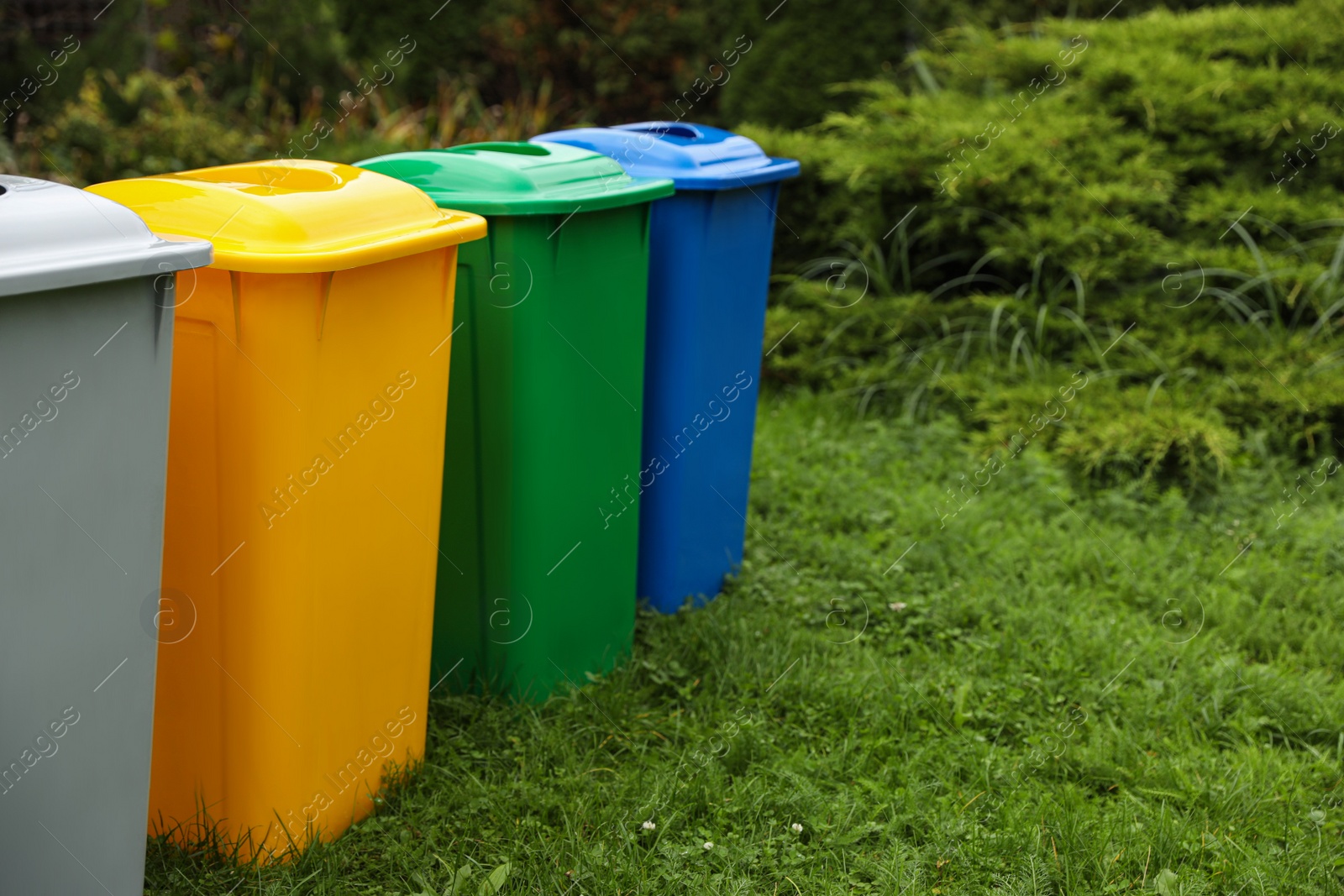 Photo of Many color recycling bins on green grass outdoors, space for text