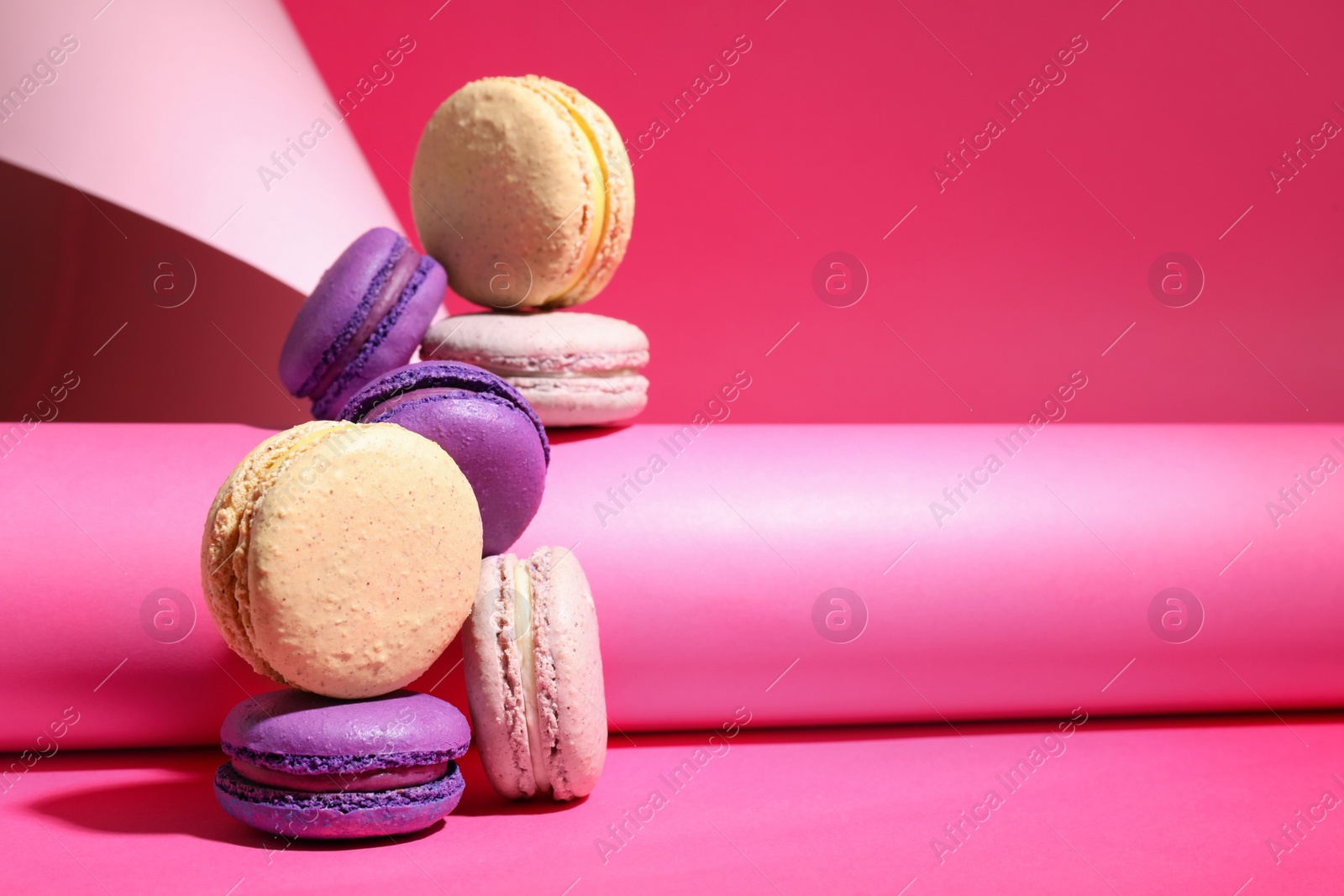 Photo of Delicious fresh colorful macarons and paper roll on pink background. Space for text