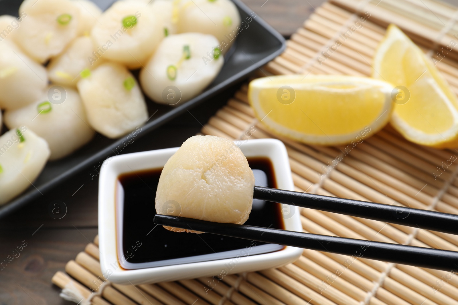 Photo of Taking raw scallop from bowl of soy sauce with chopsticks at wooden table, closeup