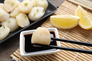 Photo of Taking raw scallop from bowl of soy sauce with chopsticks at wooden table, closeup