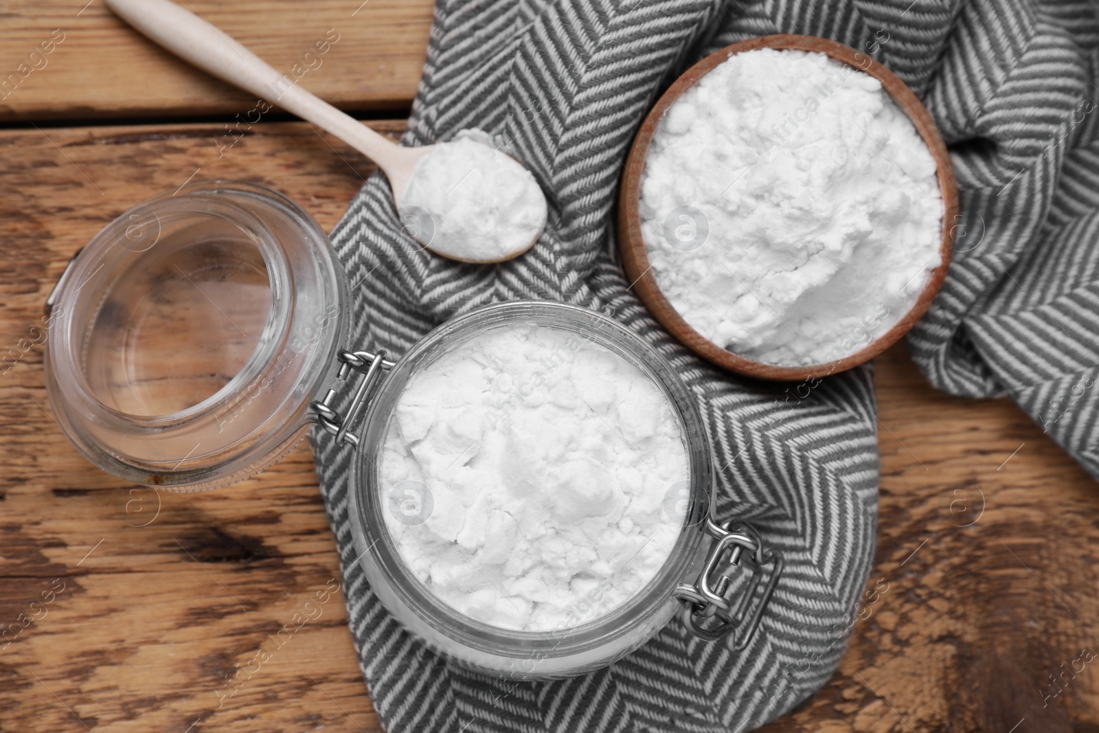 Photo of Bowl, spoon and glass jar of natural starch on wooden table, flat lay