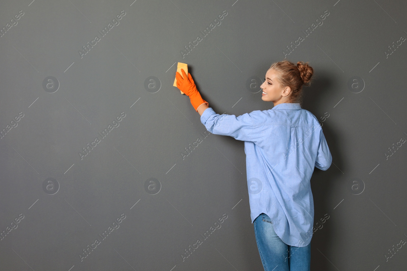 Photo of Woman in gloves cleaning grey wall with rag