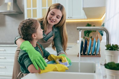 Mother and daughter in protective gloves washing plate above sink in kitchen
