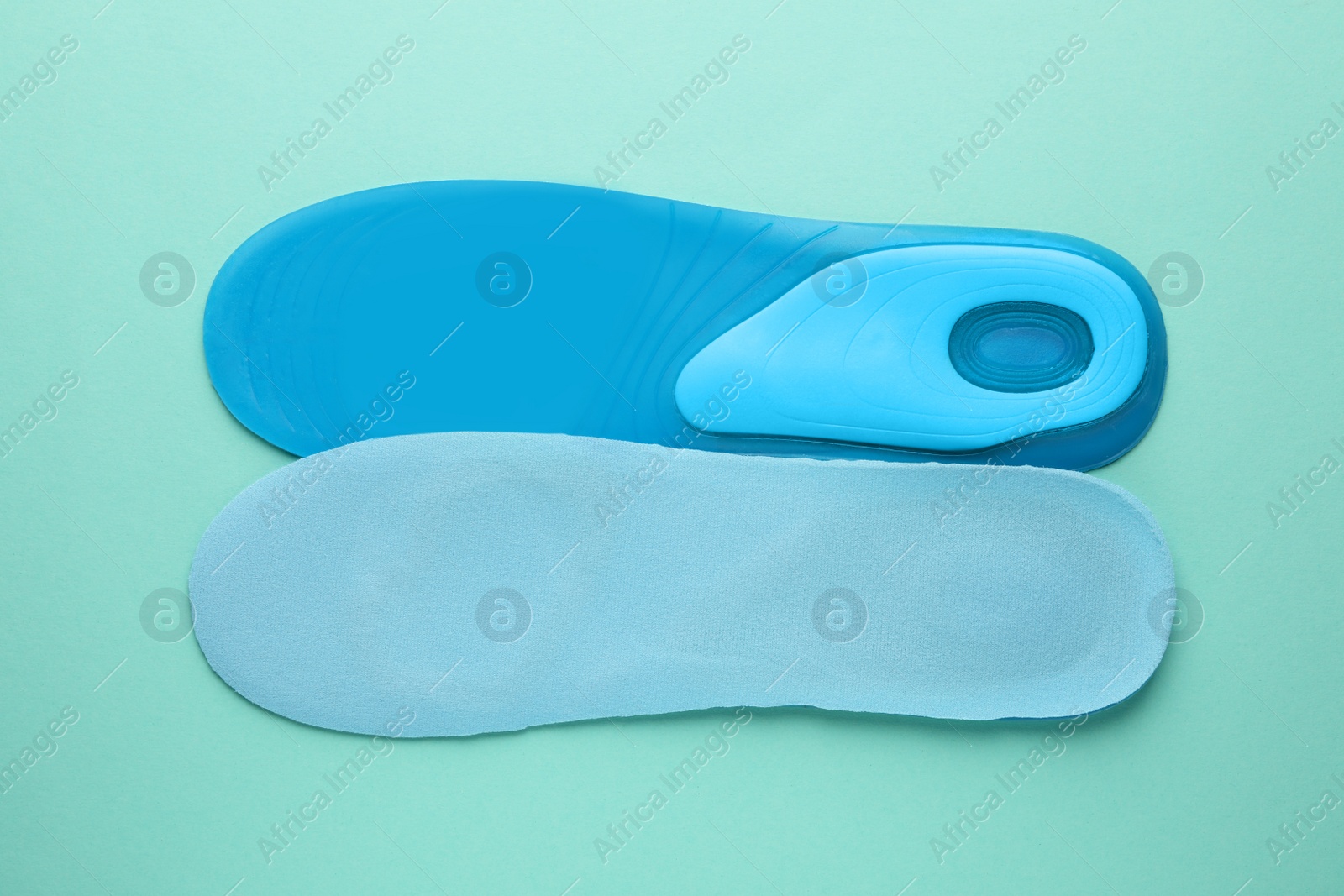 Photo of Light blue orthopedic insoles on turquoise background, flat lay