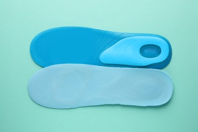 Photo of Light blue orthopedic insoles on turquoise background, flat lay