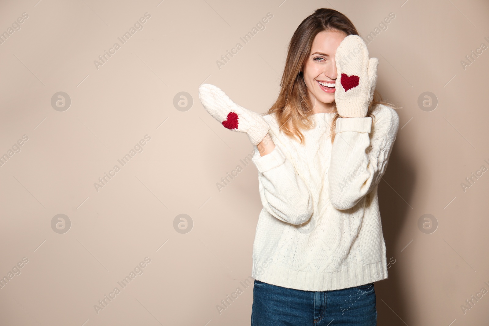 Image of Happy young woman wearing warm sweater and knitted mittens on beige background. Space for text