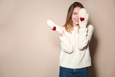 Happy young woman wearing warm sweater and knitted mittens on beige background. Space for text