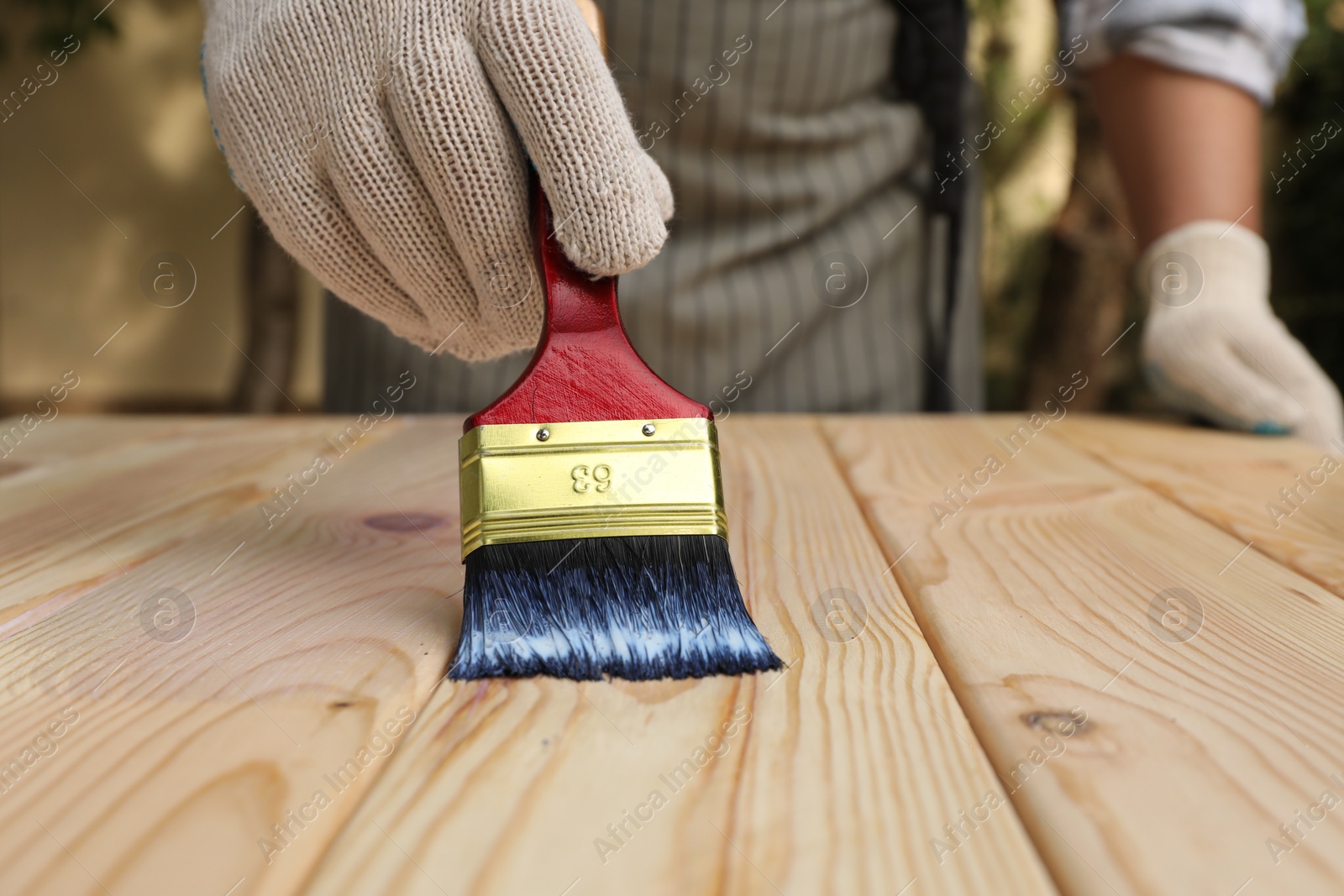 Photo of Man varnishing wooden surface with brush outdoors, closeup