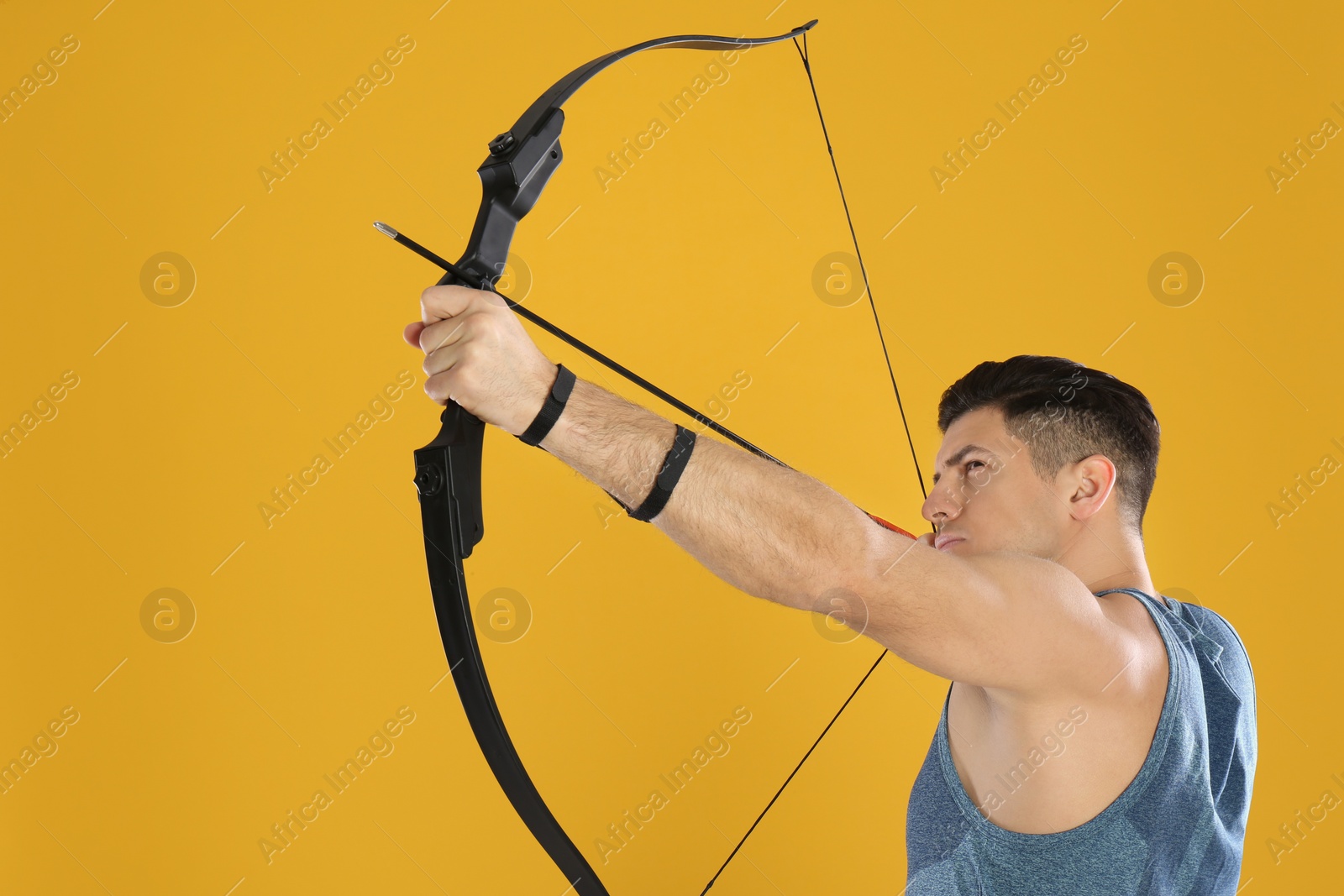 Photo of Man with bow and arrow practicing archery on yellow background