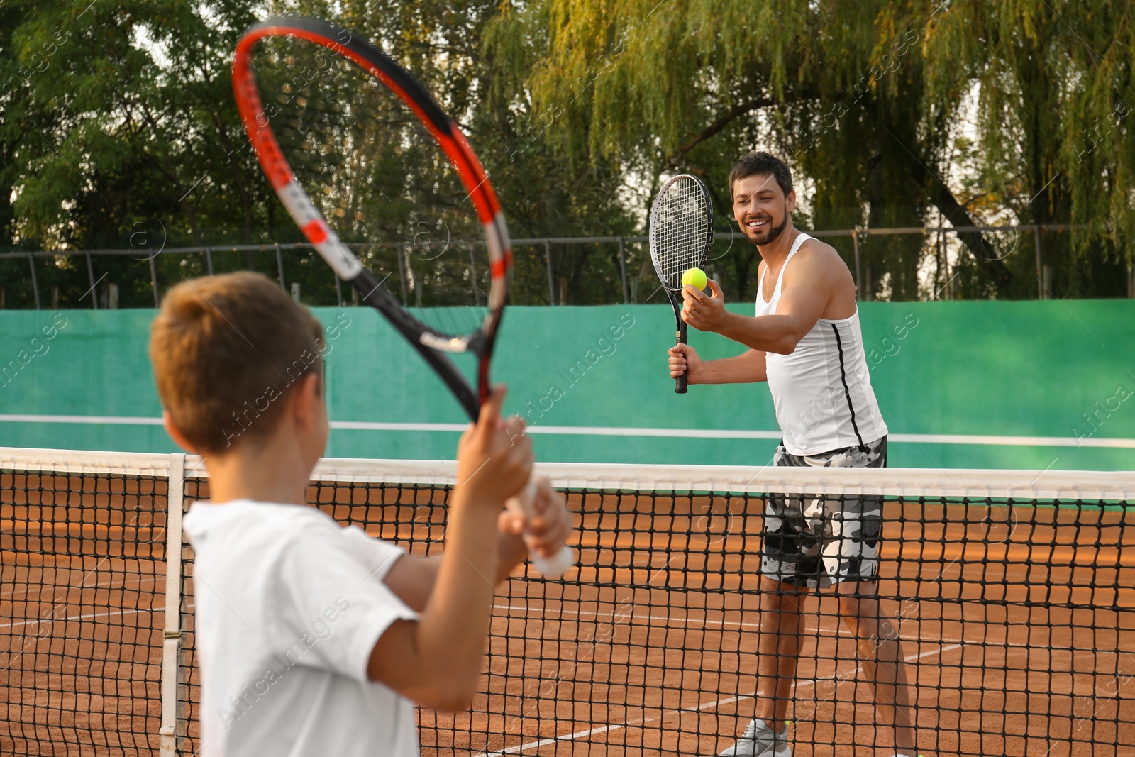 Photo of Father with his son playing tennis on court