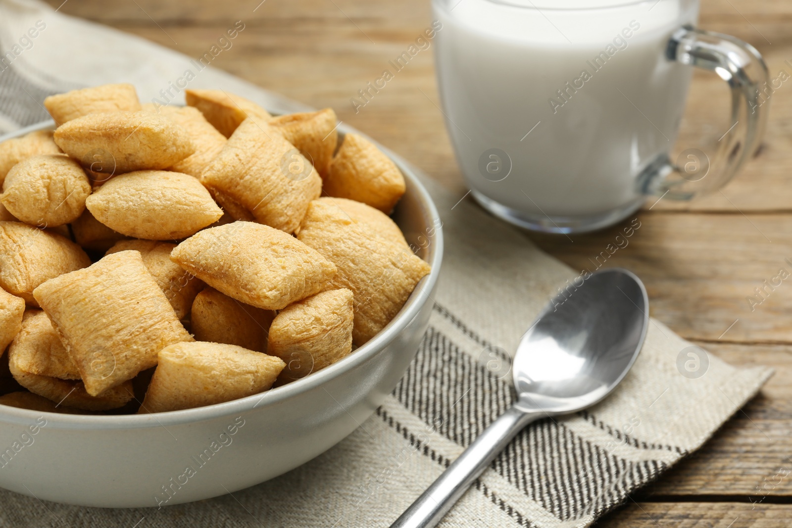 Photo of Bowl of sweet crispy corn pads and milk on wooden table, closeup. Breakfast cereal