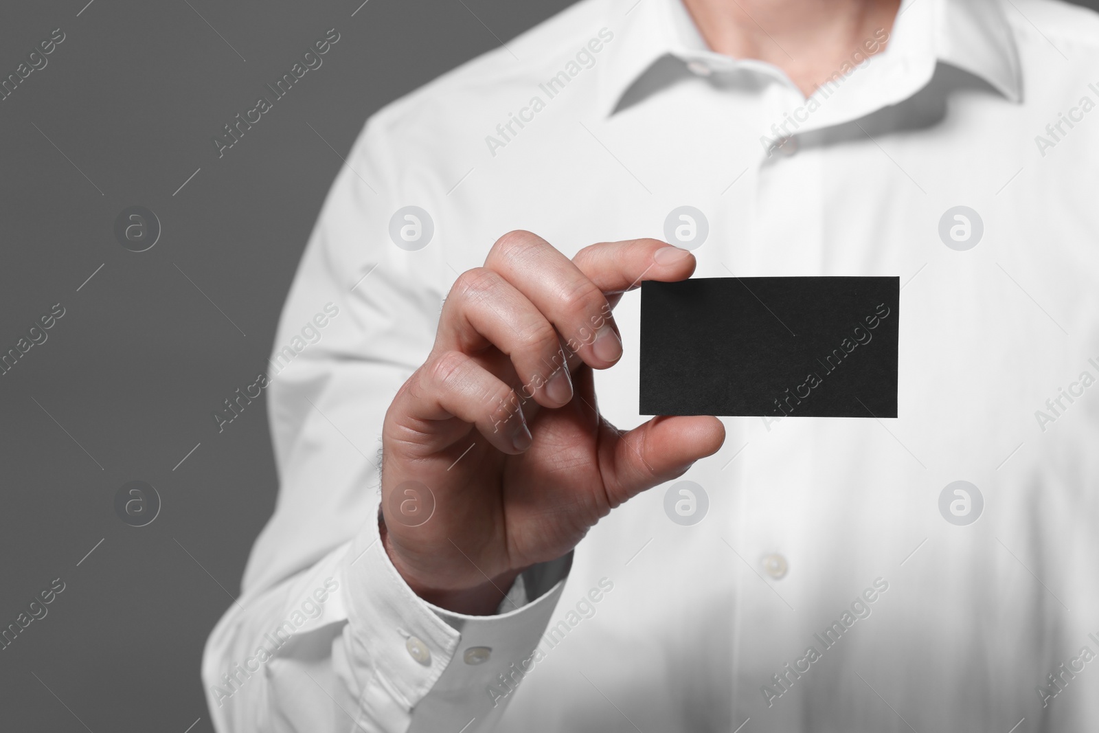 Photo of Man holding blank business card on grey background, closeup