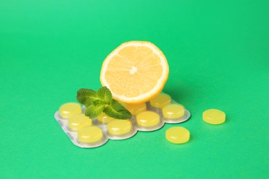 Photo of Fresh lemon, mint leaves and blister with cough drops on green background