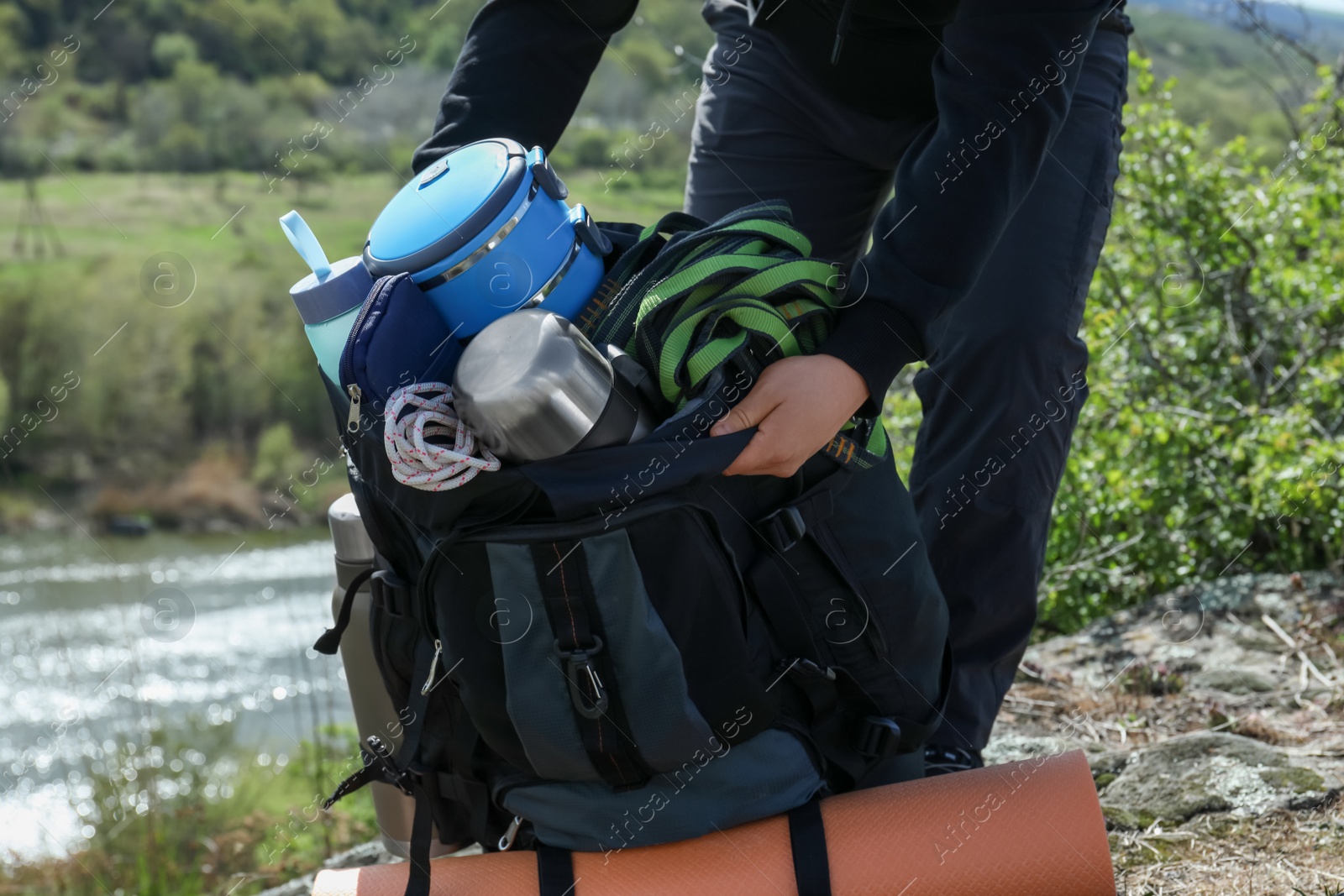 Photo of Hiker packing backpack on rocky hill near river, closeup