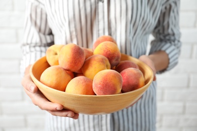 Photo of Woman holding bowl with delicious ripe peaches, closeup