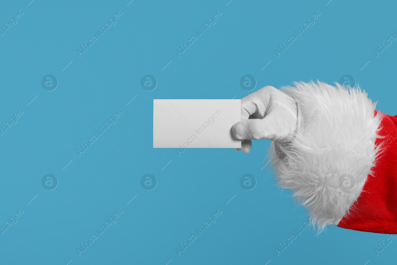 Photo of Merry Christmas. Santa Claus holding blank card on light blue background, closeup. Space for text
