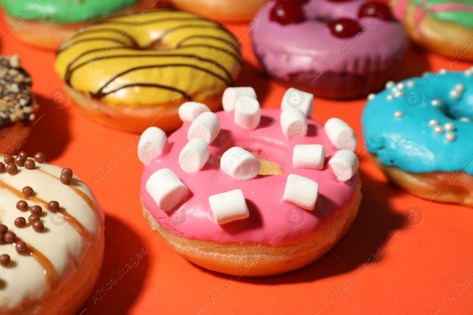 Photo of Sweet tasty glazed donuts on coral background, closeup