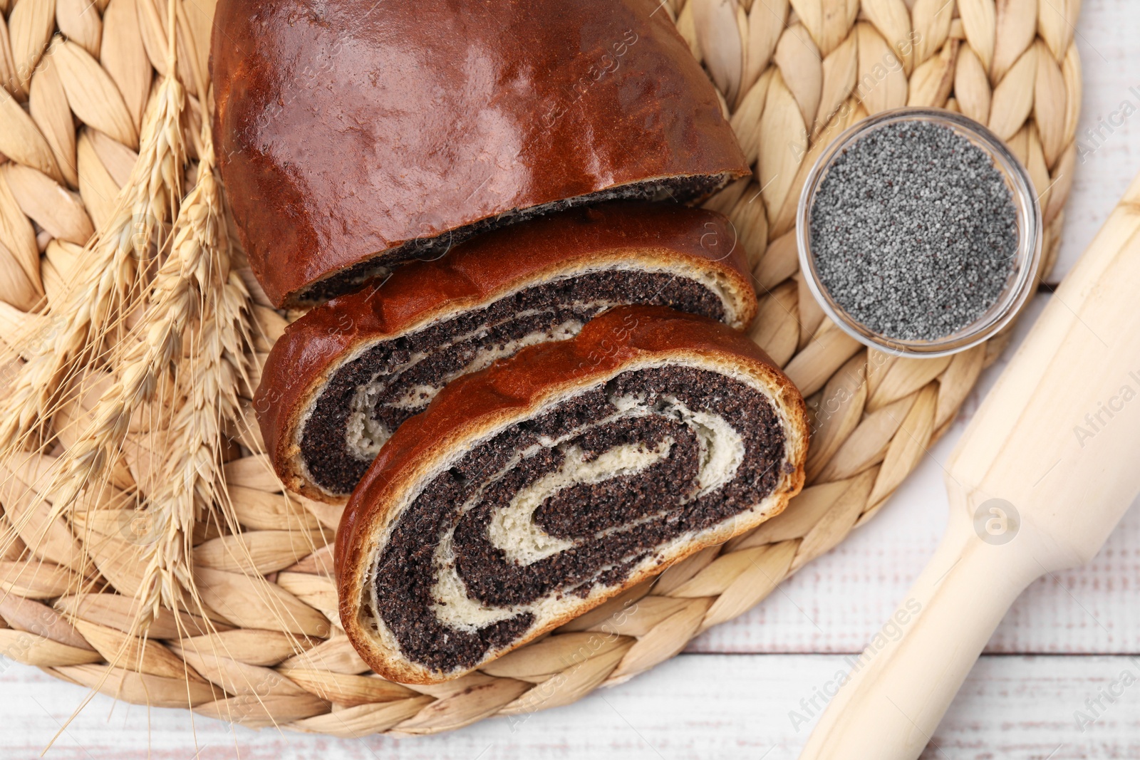 Photo of Cut poppy seed roll and spikelets on white wooden table, flat lay. Tasty cake