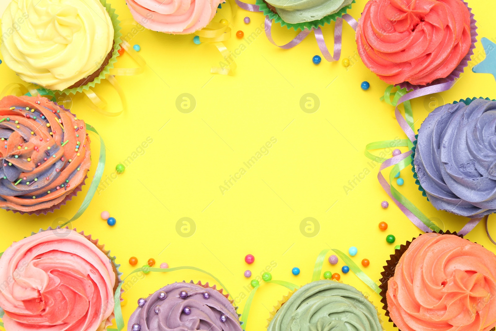 Photo of Delicious cupcakes with bright cream and party decor on yellow background, flat lay. Space for text