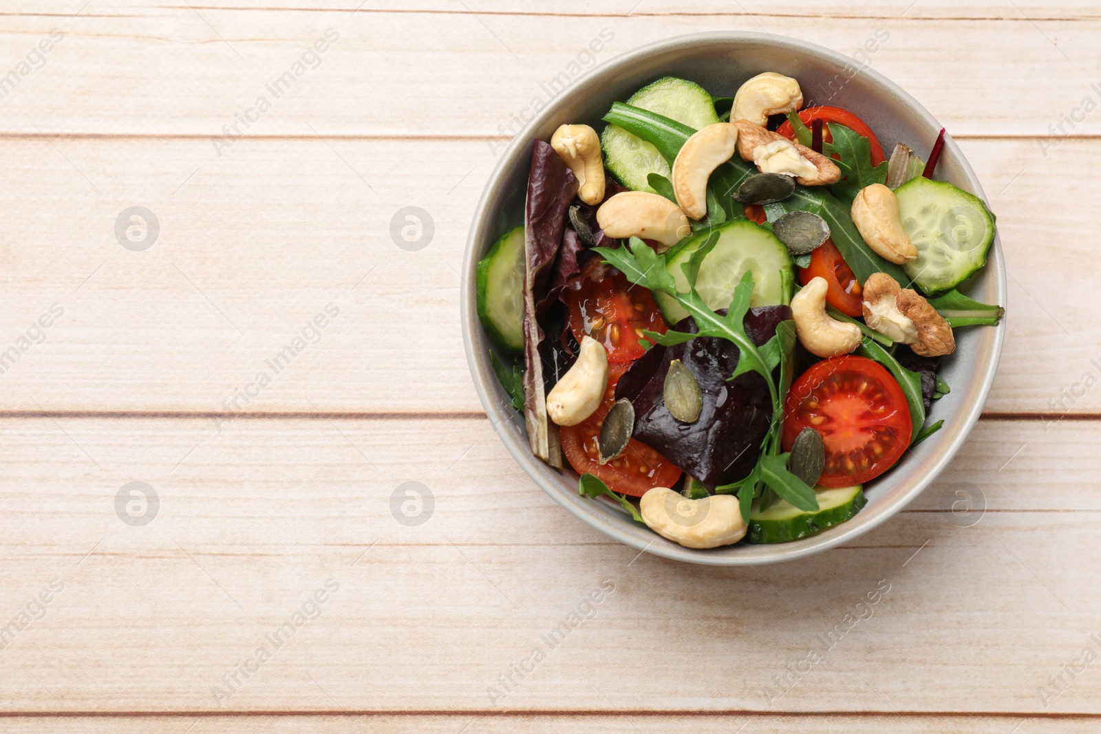 Photo of Tasty fresh vegetarian salad on light wooden table, top view. Space for text