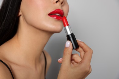 Photo of Young woman applying red lipstick on light gray background, closeup
