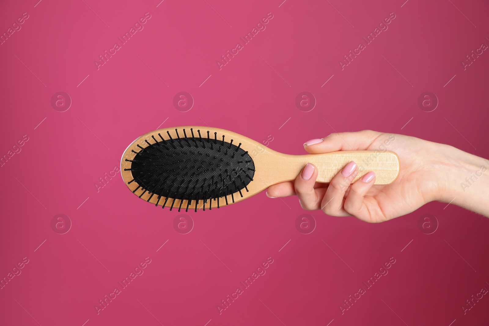 Photo of Woman holding wooden hair brush against crimson background, closeup