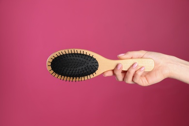 Photo of Woman holding wooden hair brush against crimson background, closeup