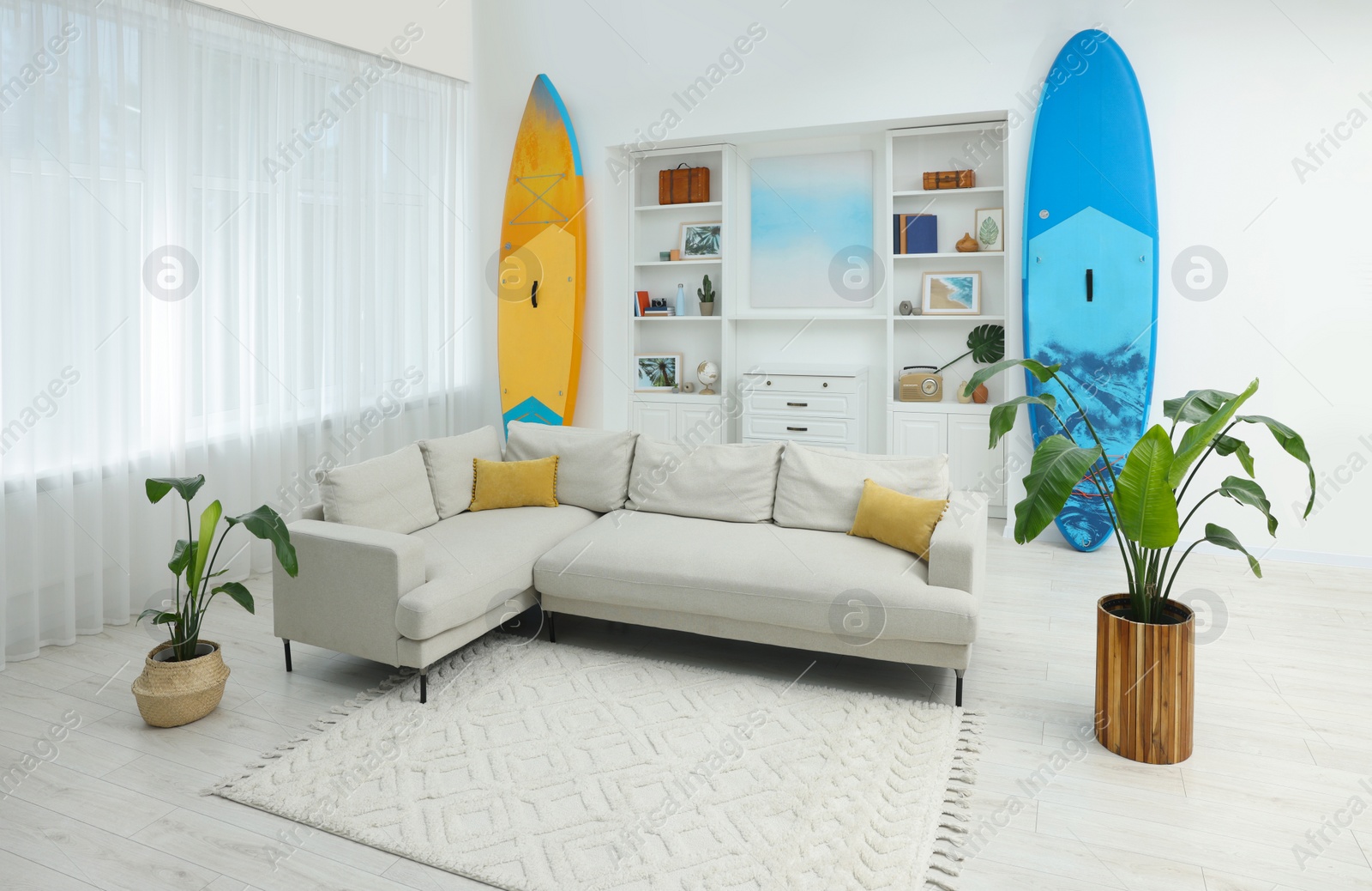 Photo of SUP boards, shelving unit with different decor elements and stylish sofa in room. Interior design