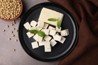 Delicious tofu cheese, basil and soybeans on brown textured table, flat lay