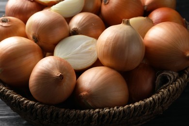 Whole and cut onions on black wooden table, closeup