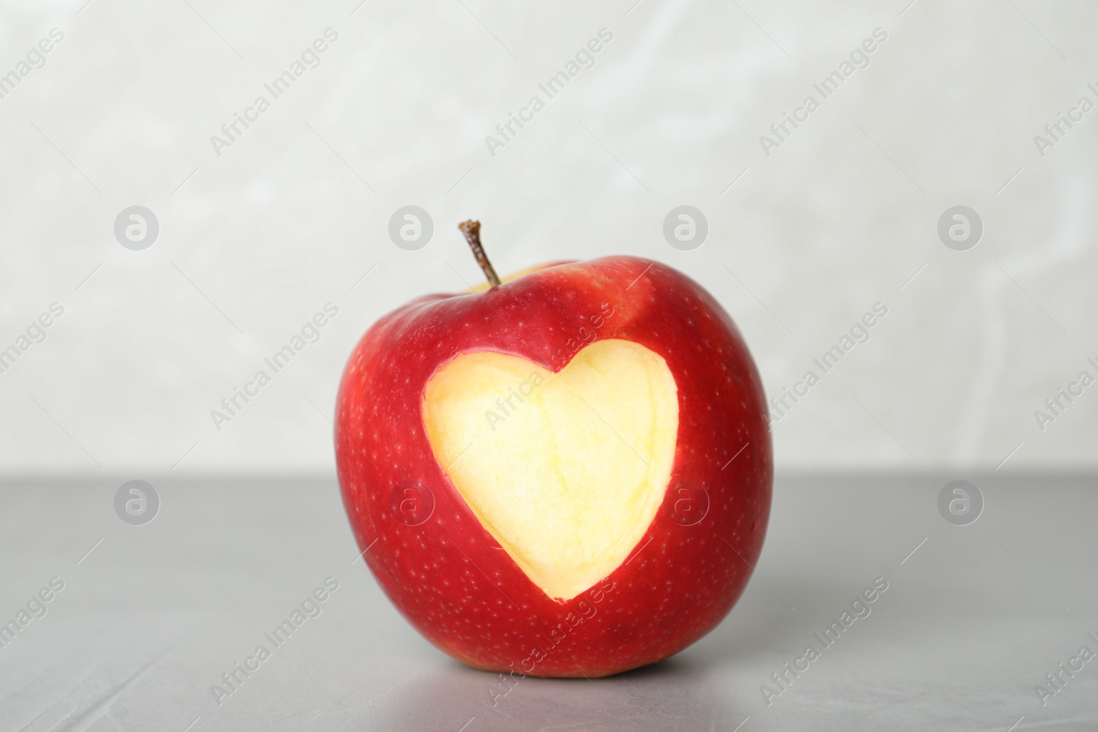 Photo of Red apple with carved heart on table against light background
